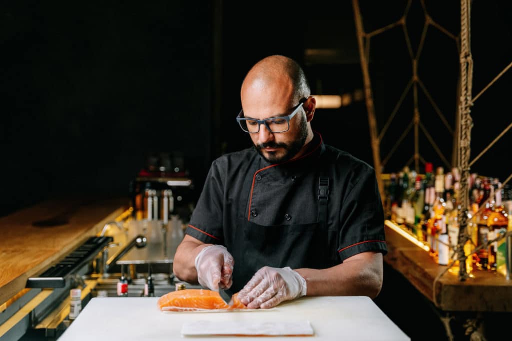 Photo of a chef with eyeglasses slicing sashimi